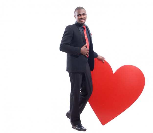 Полная длина портрет молодого африканского человека в черном сюите и красном галстуке, опираясь на большое украшенное красное сердце