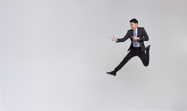 Full length Asian business man running jumping in air and pointing finger to copy space