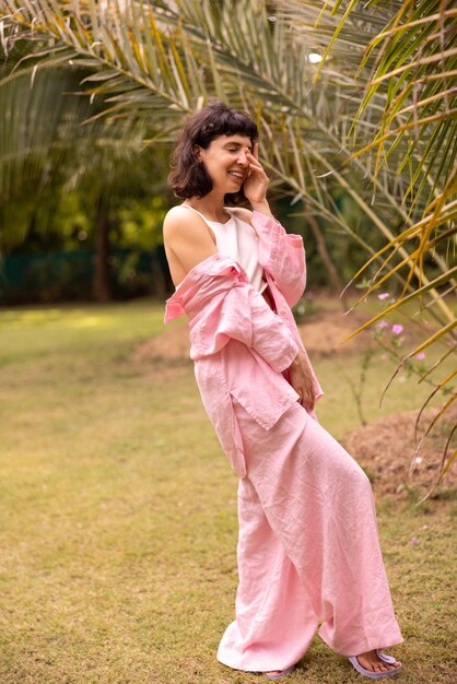 Full length attractive caucasian young brunette in pink suit laughs with eyes closed and covering face standing in garden People sincere emotions lifestyle concept