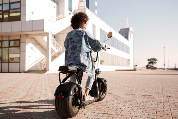 Full-length back view image of young woman rides on motorbike