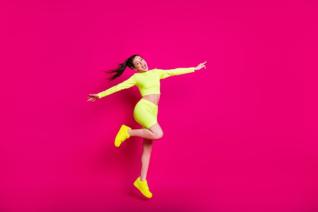 활기찬 분홍색 배경에 격리된 카피스페이스를 즐겁게 가리키며 웃고 있는 점프하는 스포츠우먼의 전신 크기 사진