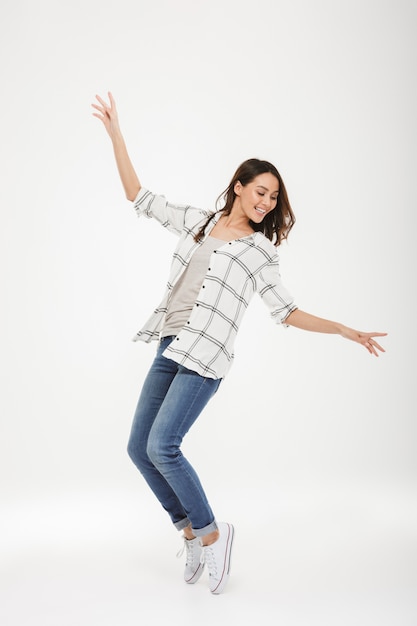 Full length Cheerful brunette woman in shirt dancing over gray