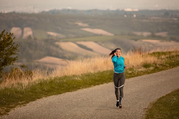 Full length of female runner listening music while jogging on the road at dawn