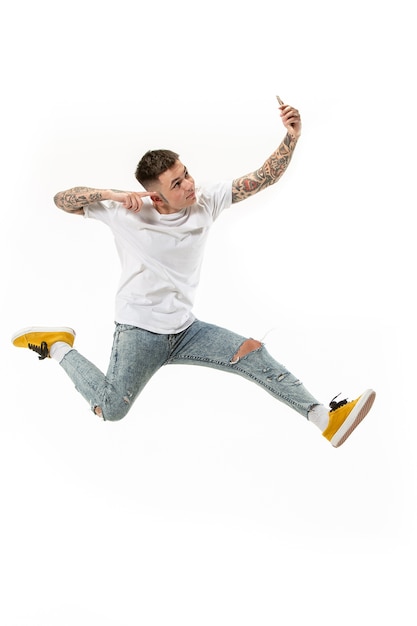 Free photo full length of handsome young man taking phone while jumping against orange studio background.