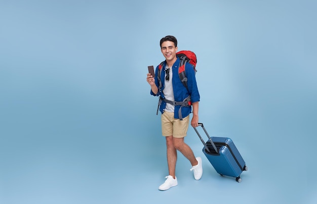 Full length Happy smiling young tourist Asian man walking while holding luggage and showing passport