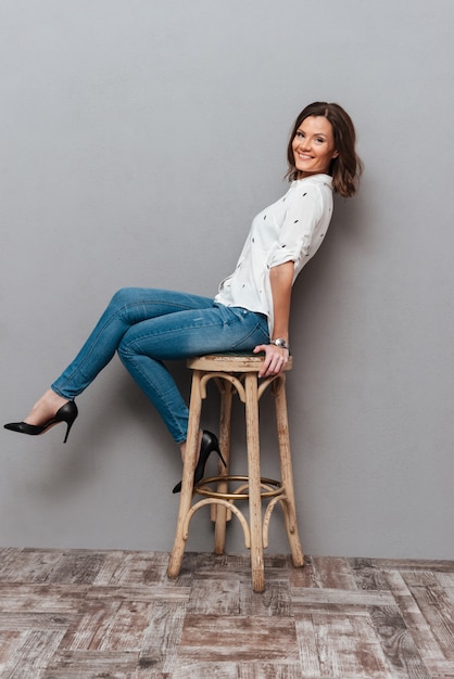 Full length of happy woman posing on chair and looking at the camera