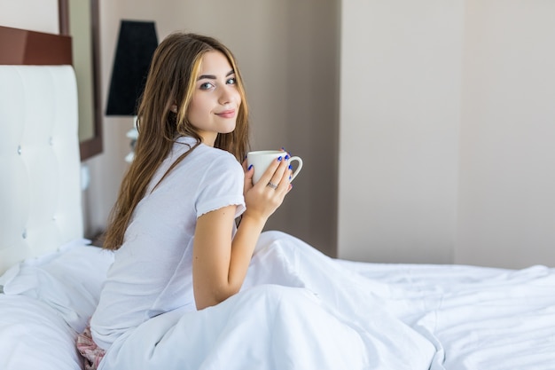 Full length of happy young woman having coffee on bed