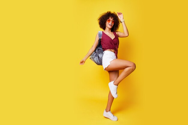 Full length image of happy active mixed race woman jumping on yellow