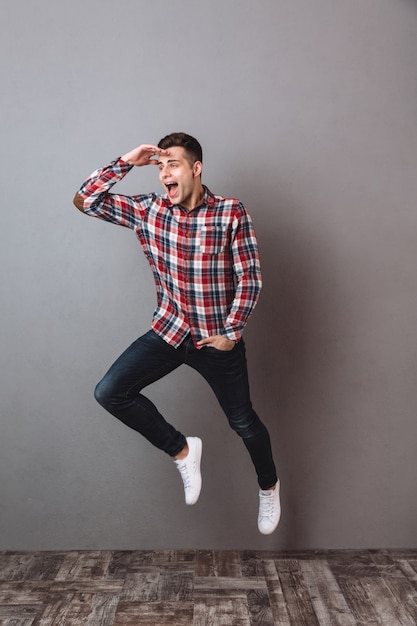 Free photo full length image of happy man in shirt and jeans jimping and looking away with arm in pocket