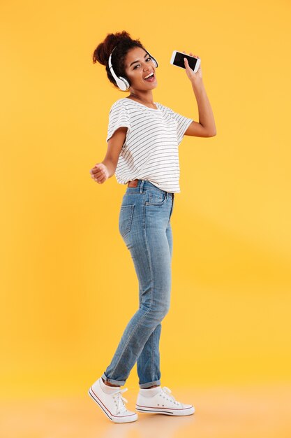 Full-length image of pleased african woman dancing and listening music