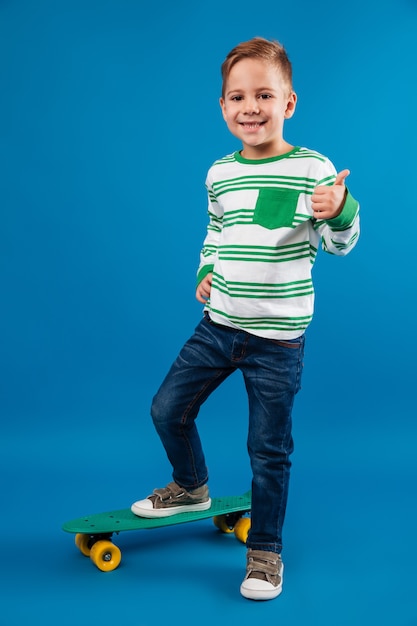 Free photo full length image of pleased young boy posing with skateboard