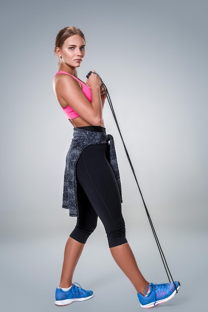 Full length image of a pretty fitness woman doing exercise with skipping rope over gray background. Young woman with beautiful slim healthy body posing in studio.