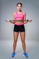 Free photo full length image of a pretty fitness woman doing exercise with skipping rope over gray background. young woman with beautiful slim healthy body posing in studio.