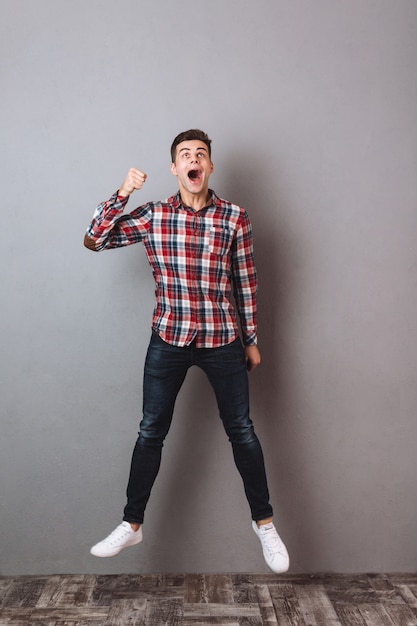 Full length image of Screaming man in shirt and jeans jumping and looking up