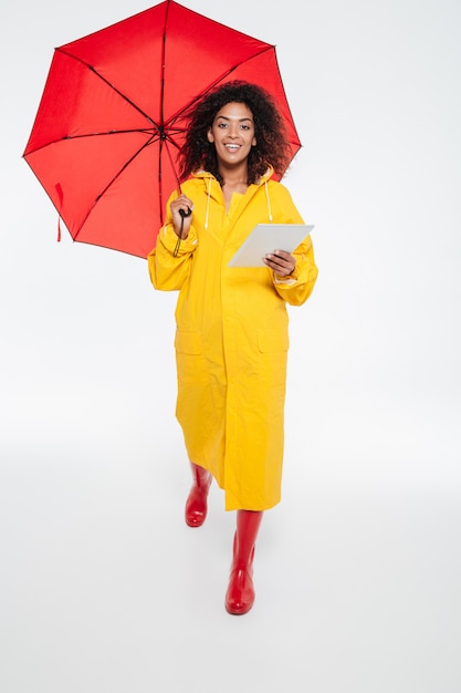 Full length image of smiling african woman in raincoat