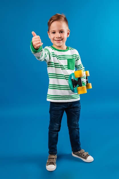 Full length image of smiling young boy holding skateboard