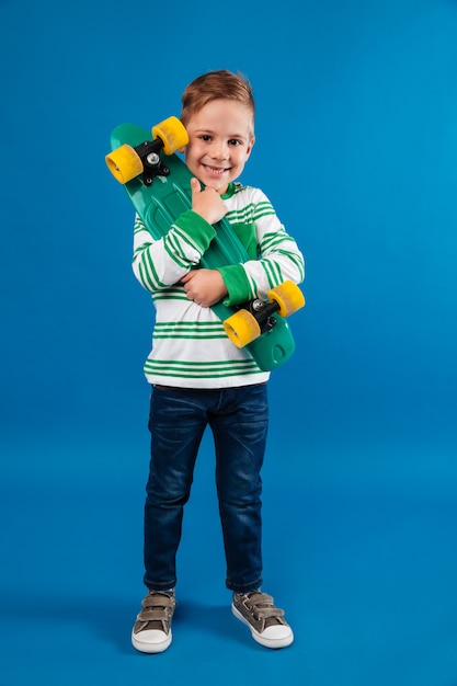 Full length image of smiling young boy hugging skateboard