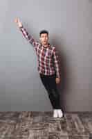 Free photo full length image of surprised man in shirt and jeans holding copyspace in hand and looking