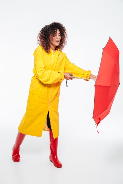Free photo full-length image of young african woman in raincoat opening umbrella