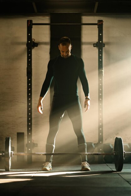 Мужчина в полный рост мускулистого телосложения концентрируется перед подъемом штанги во время силовых тренировок в спортзале