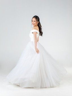 곧 신부가 될 젊은 매력적인 아시아 여성의 전체 길이가 행복해 보이는 하얀 웨딩 드레스를 입고 있습니다. 사전 결혼식 사진에 대한 개념입니다.