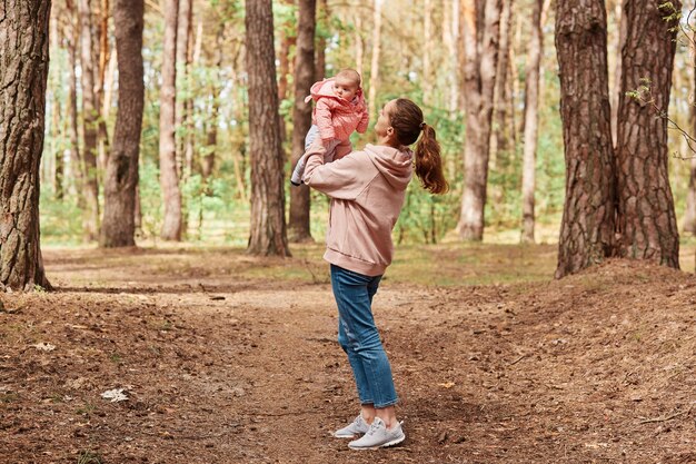 Full length outdoor shot of loving woman throwing up her infant daughter in air