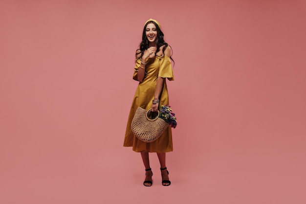 Free photo full length photo of modern woman with wavy black hair in fashionable bright yellow outfit and dark shoes looking into camera