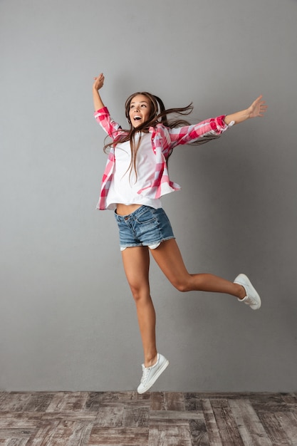 Полнометражное фото милой молодой женщины в наушниках слушая музыку и скача