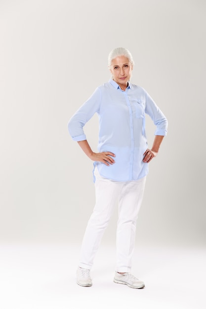 Full-length photo of serious senior gray-haired woman, standing with hands on her waist