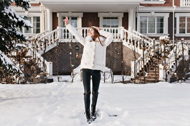 Full-length photo of slim young woman in warm stylish clothes enjoying winter weekend. Outdoor portrait of fascinating caucasian lady in dark pants posing with hands up in cold day..