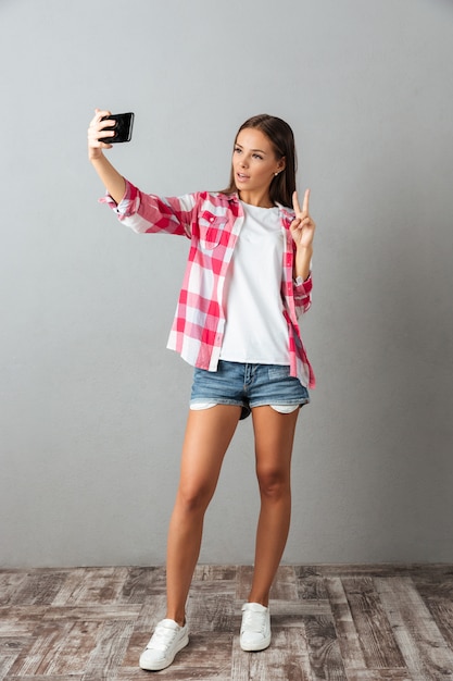 Full-length photo of young beautiful woman, taking selfie photo by her phones