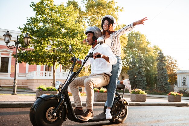 通りでモダンなバイクに乗って幸せなアフリカのカップルの全身写真