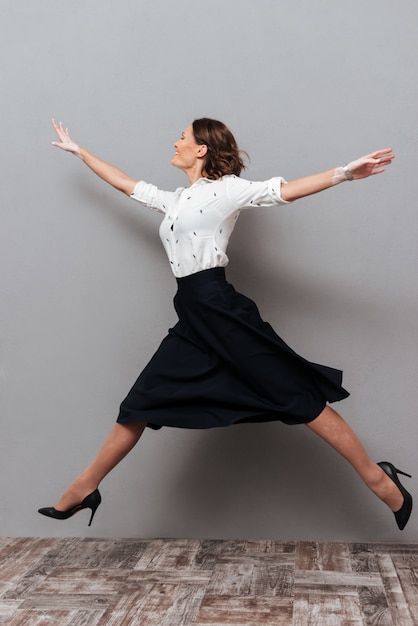 Free photo full length picture of woman in business clothes jumping and running in studio on gray