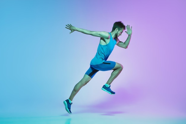 Full length portrait of active young caucasian running, jogging man on in neon