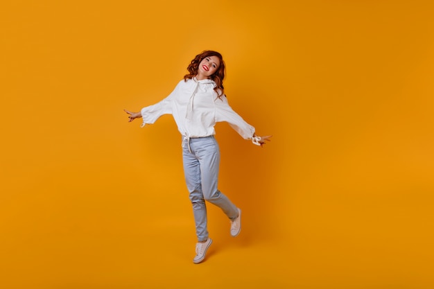 Free photo full-length portrait of amazing slim girl with ginger hair. caucasian romantic woman dancing on yellow wall.