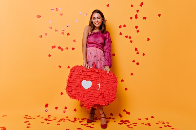 Free photo full-length portrait of appealing girl standing on orange with confetti. enchanting woman in pink dress having fun.