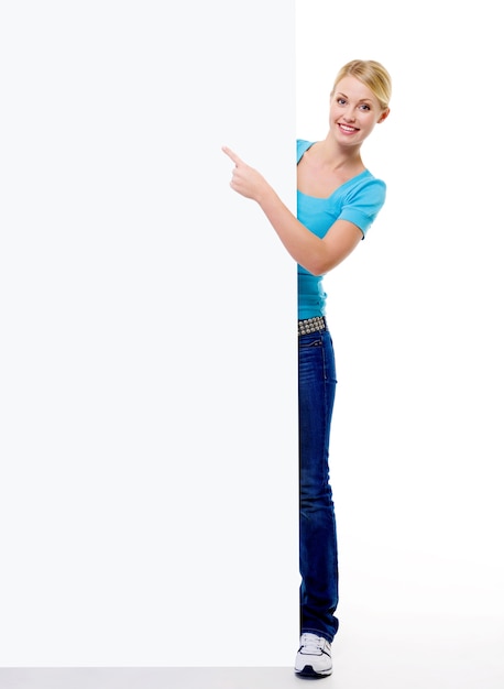 Free photo full-length portrait of a beautiful blonde female person points  on the blank billboard - isolated on white