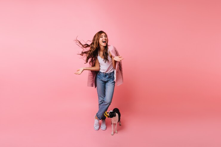 Free Photo full-length portrait of brunette lady in jeans posing with dog. indoor portrait of beautiful female model standing beside french bulldog.