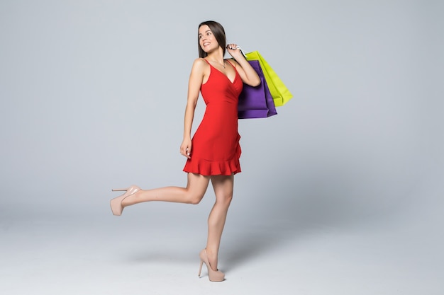 Full length portrait of a cheerful attractive woman holding shopping bag isolated on a white wall