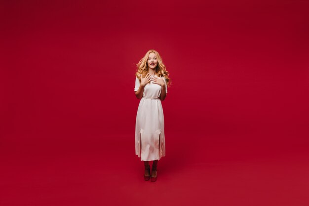 Полнометражный портрет жизнерадостной женщины в белом платье. очаровательная длинноволосая девушка изолирована на красной стене.