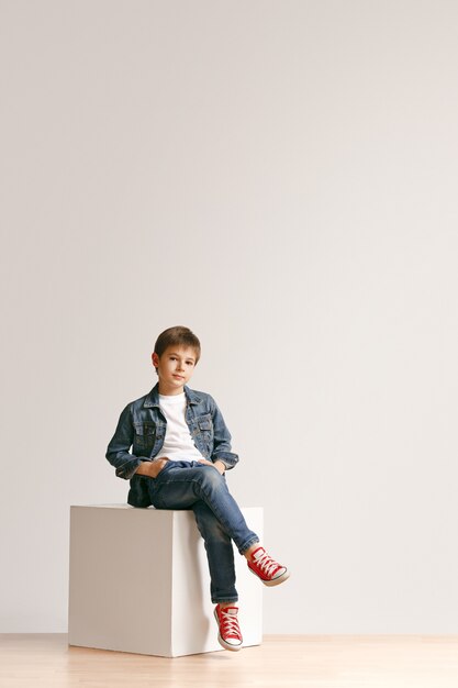 Full length portrait of cute little kid boy in stylish jeans clothes and smiling, standing on white. Kids fashion concept