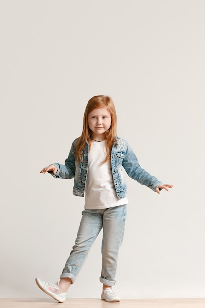カメラ目線と笑顔のスタイリッシュなジーンズ服でかわいい小さな子供の完全な長さの肖像画