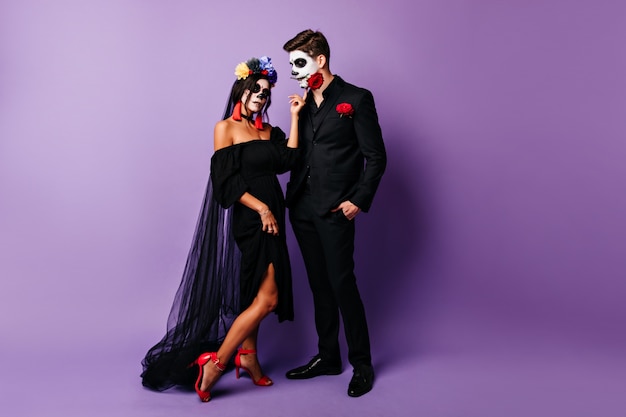 Full-length portrait of dead bride posing on purple background. Studio photo of spooky couple celebrating halloween.