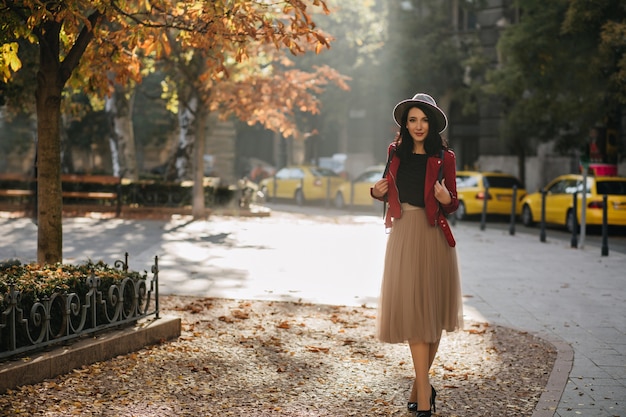 Full-length portrait of enchanting brunette woman standing on the street in sunny day