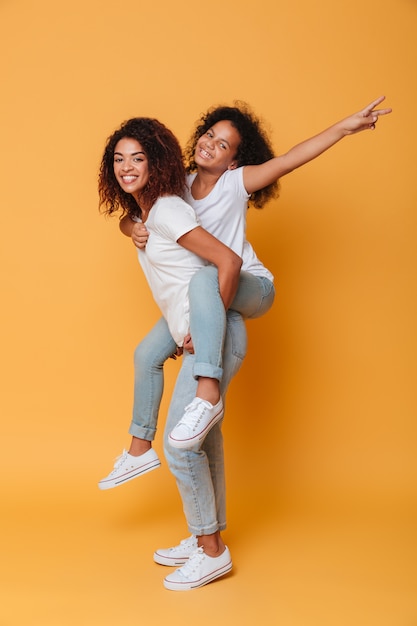 Free photo full length portrait of an excited african girl carrying little sister