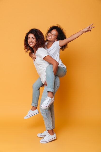 Full length portrait of an excited african girl carrying little sister