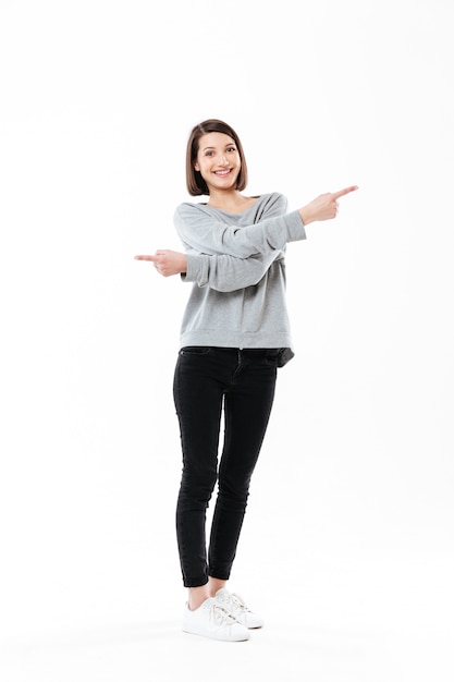 Full length portrait of an excited happy woman pointing fingers both ways isolated over white 