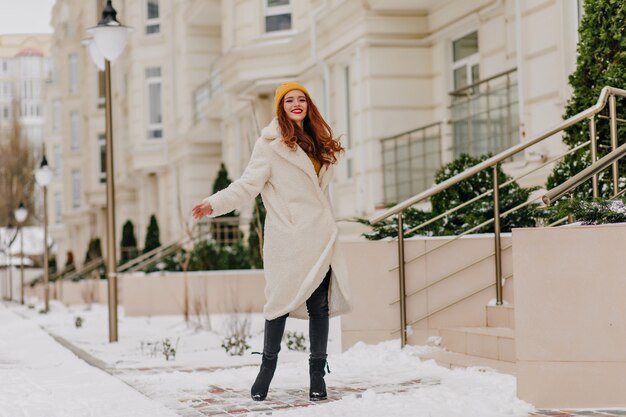 Full-length portrait of fashionable ginger woman smiling in cold december day. Glad caucasian girl enjoying winter.