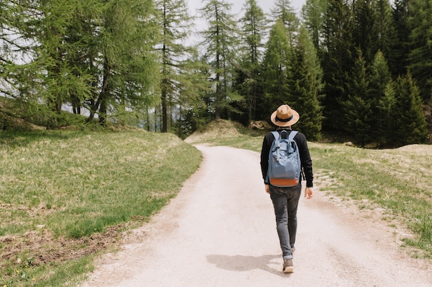 Full-length portrait from back of male traveler exploring summer forest in vacation