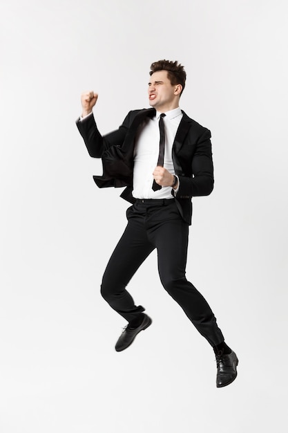 Full length Portrait Funny cheerful businessman jumping in air over gray background